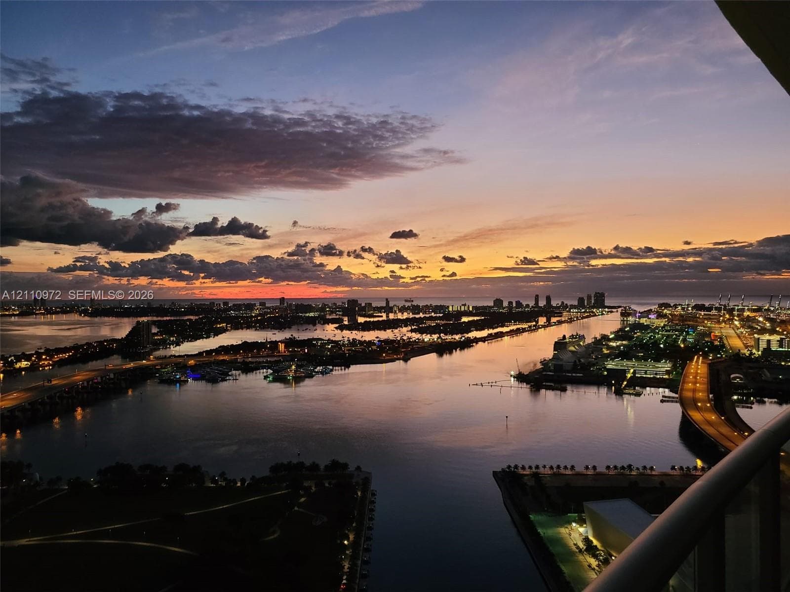 Elevated balcony featuring a panoramic cityscape, waterfront scenery, and horizon sunset