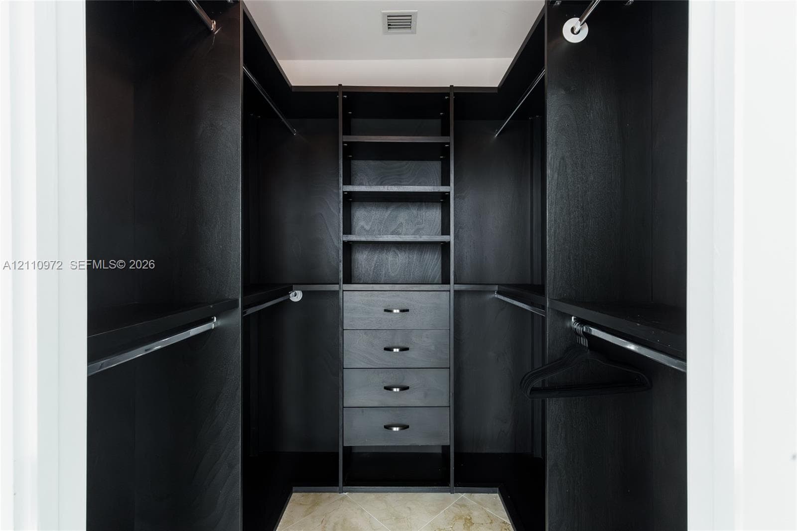 Custom walk-in closet featuring dark wood-finish cabinetry, built-in shelving, four integrated storage drawers, and polished metal hardware