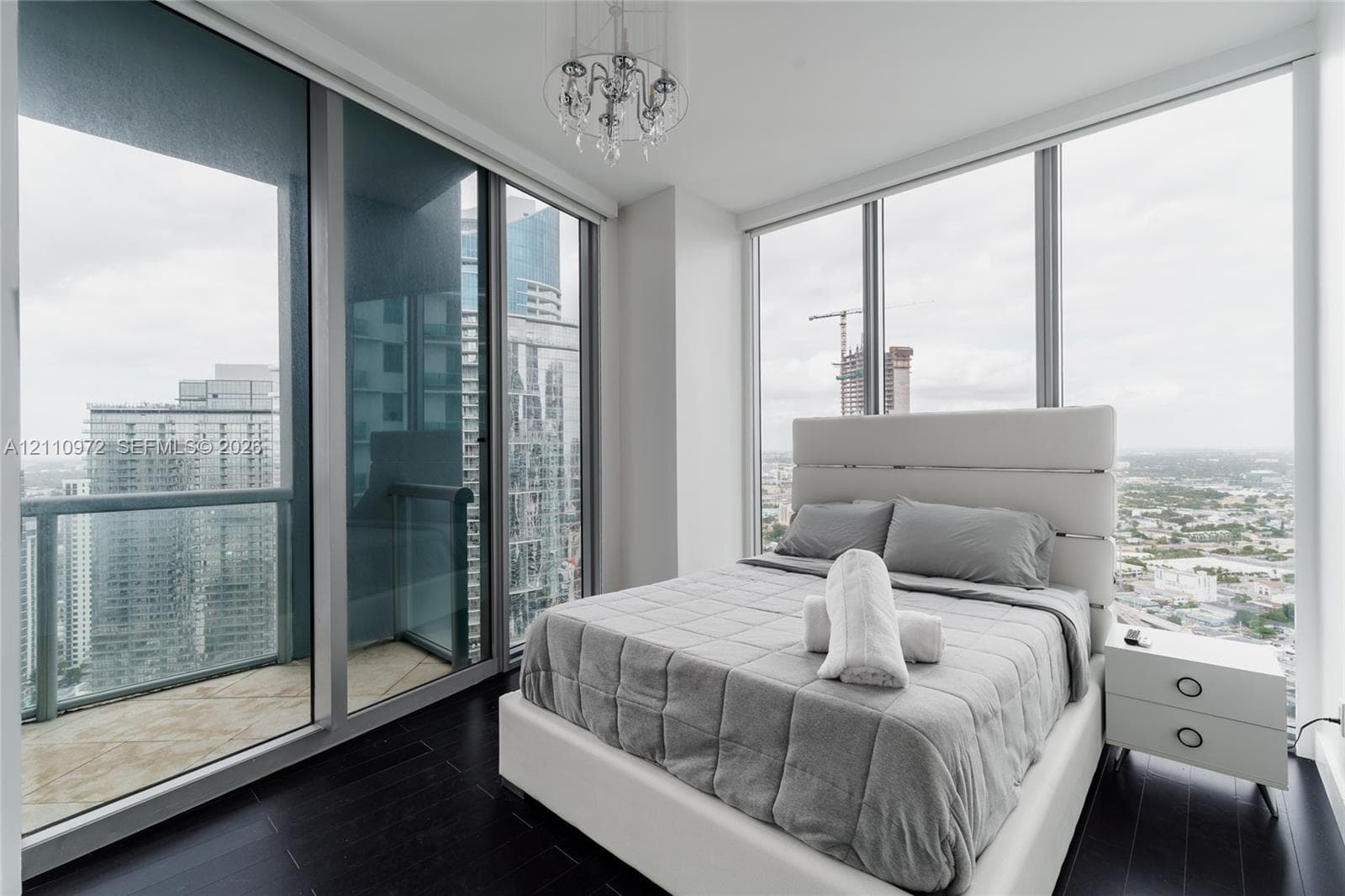 Floor-to-ceiling windows, dark wood-finish flooring, glass-railed balcony, and a multi-tiered crystal chandelier