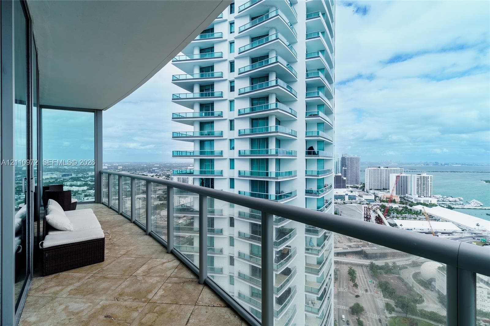 Covered outdoor balcony featuring stone tile flooring and glass railings