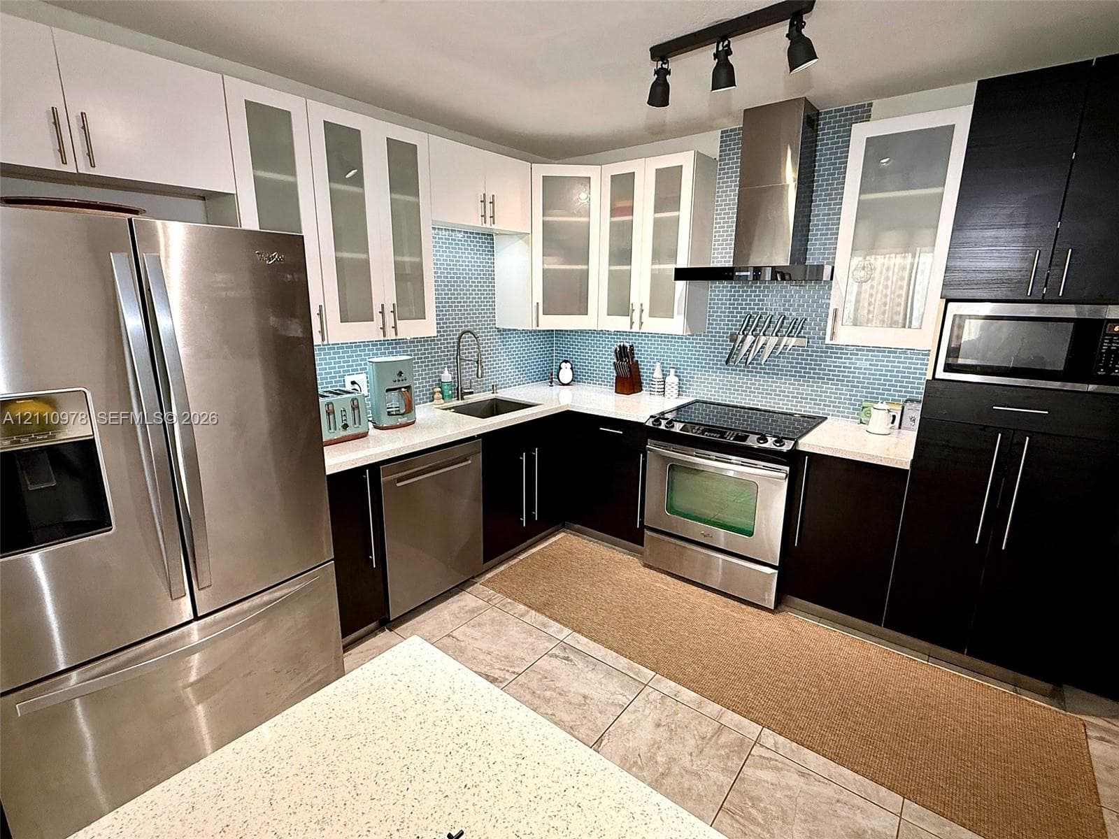 Kitchen featuring dual-tone cabinetry, stainless steel appliances, blue glass tile backsplash, stone-surface countertops, and track lighting