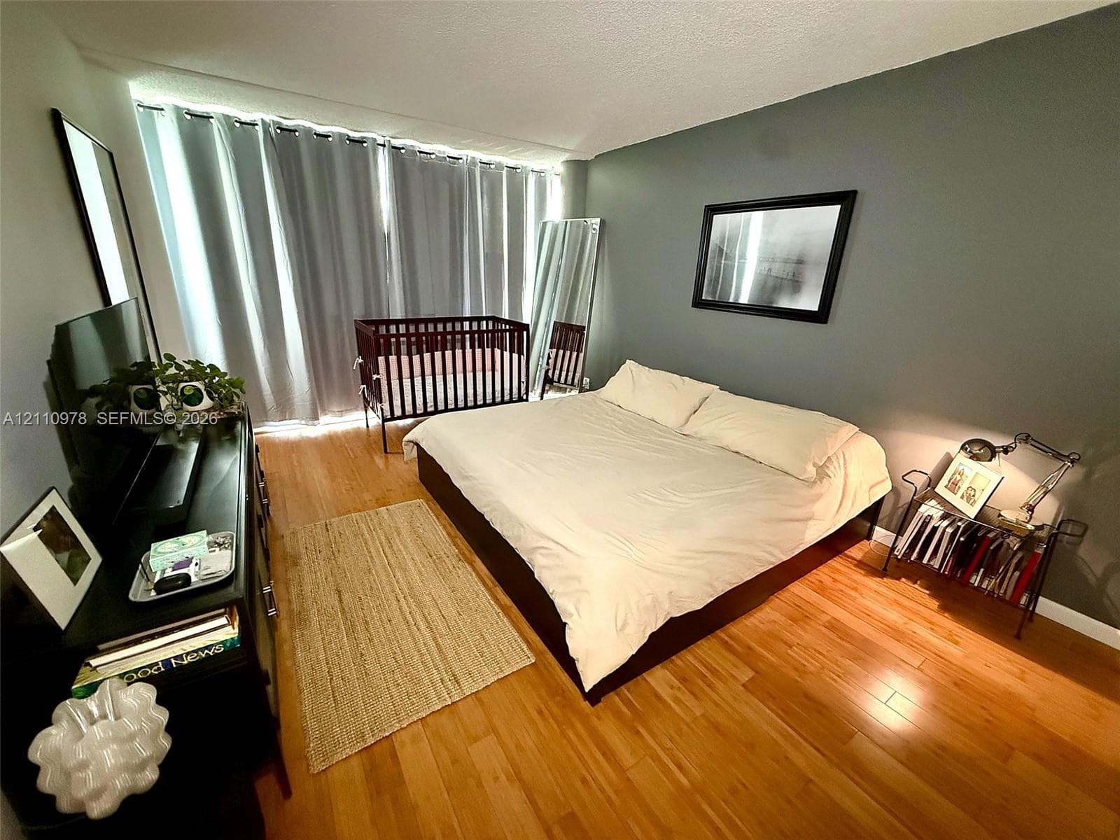 Bedroom featuring wood-finish flooring, a wall-to-wall window covered by floor-to-ceiling drapery, and a neutral-toned accent wall