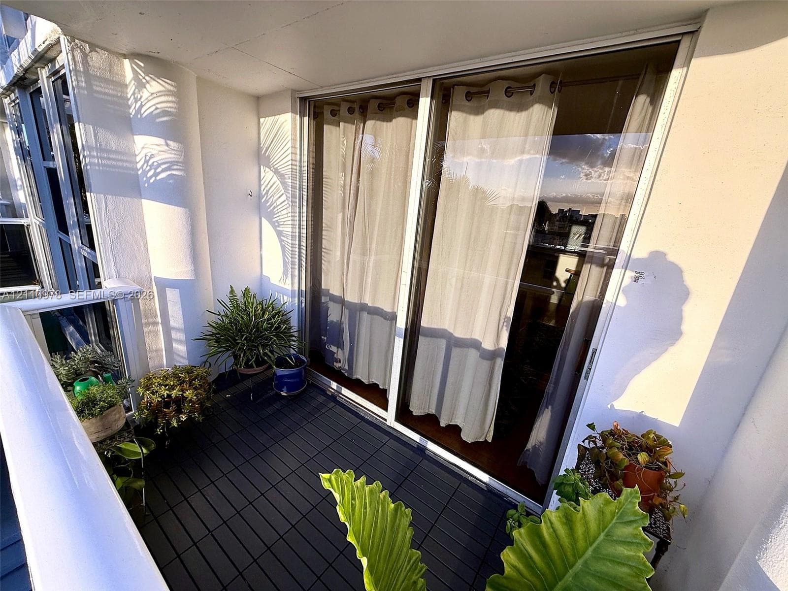 Private balcony featuring interlocking modular decking and a white railing with glass panels, accessible through large sliding glass doors