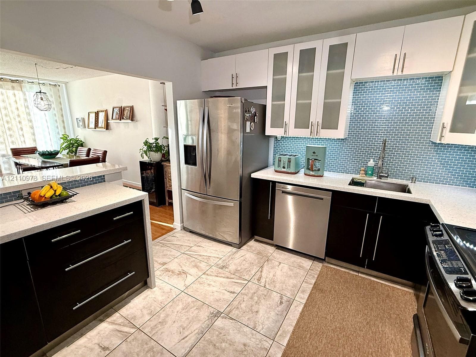 Kitchen featuring high-contrast dark lower cabinetry with white upper cabinets, quartz countertops, a blue glass tile backsplash, and stainless steel appliances
