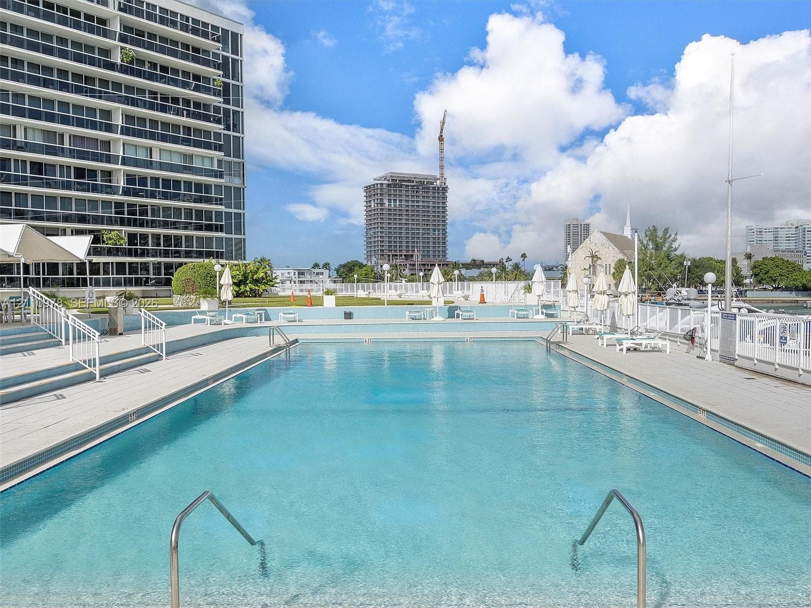 In-ground swimming pool featuring a concrete deck, metal handrails, and surrounding metal perimeter fencing