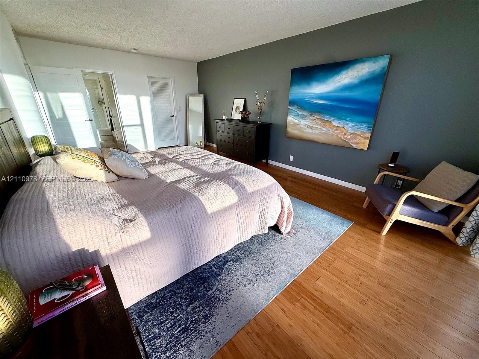 Bedroom featuring wood-finish flooring, a dark-toned accent wall, and multiple closet doors with louvered panels