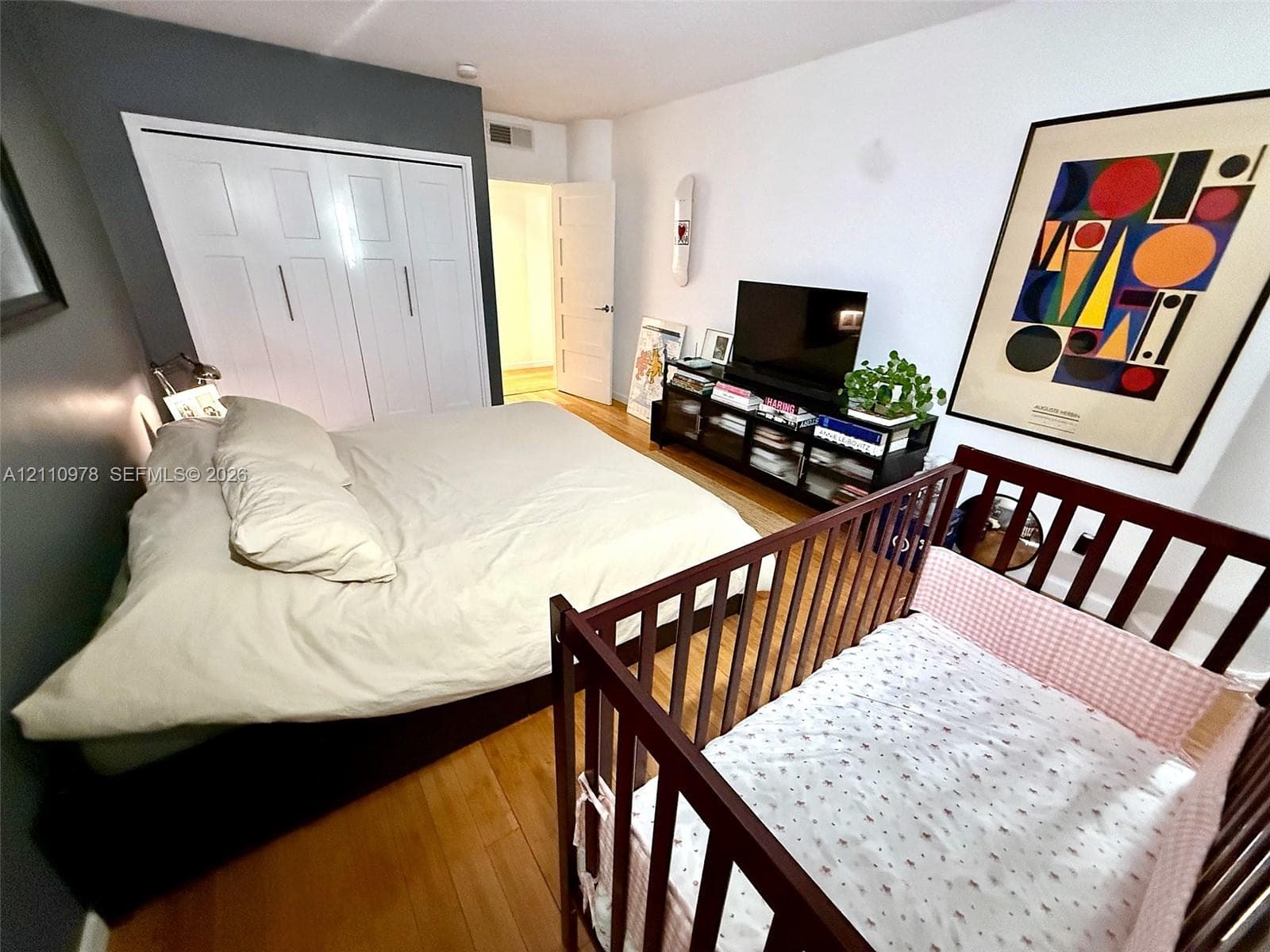 Room featuring wood-finish flooring, floor-to-ceiling four-panel closet doors with vertical hardware, and a solid-core interior door