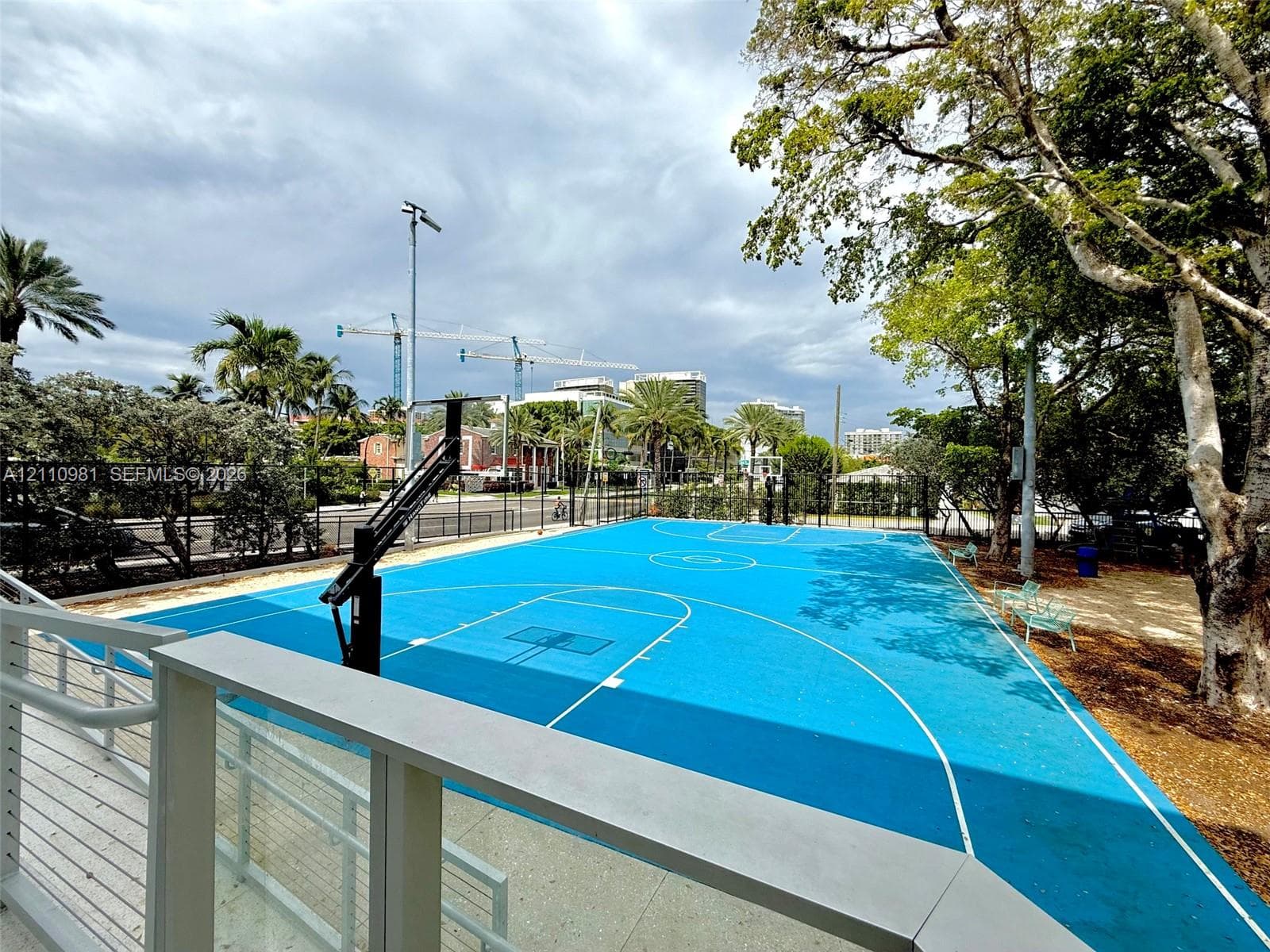 Outdoor basketball court featuring a vibrant blue court surface, an adjustable hoop system, and cable-railing perimeter enclosure