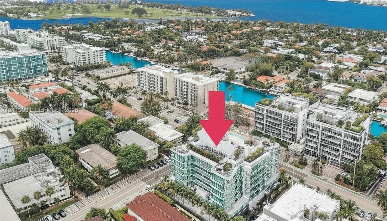 Aerial perspective of a multi-story residential building featuring extensive glass-paneled balconies, a rooftop swimming pool, terrace landscaping, and dedicated surface parking