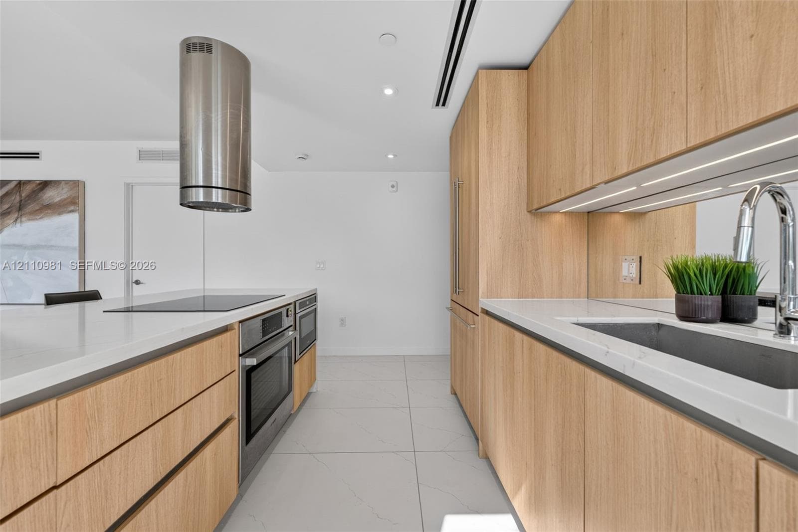 Modern kitchen featuring wood-finish cabinetry, stone-surface countertops, a stainless steel cylindrical range hood, integrated oven and cooktop, and mirrored backsplash