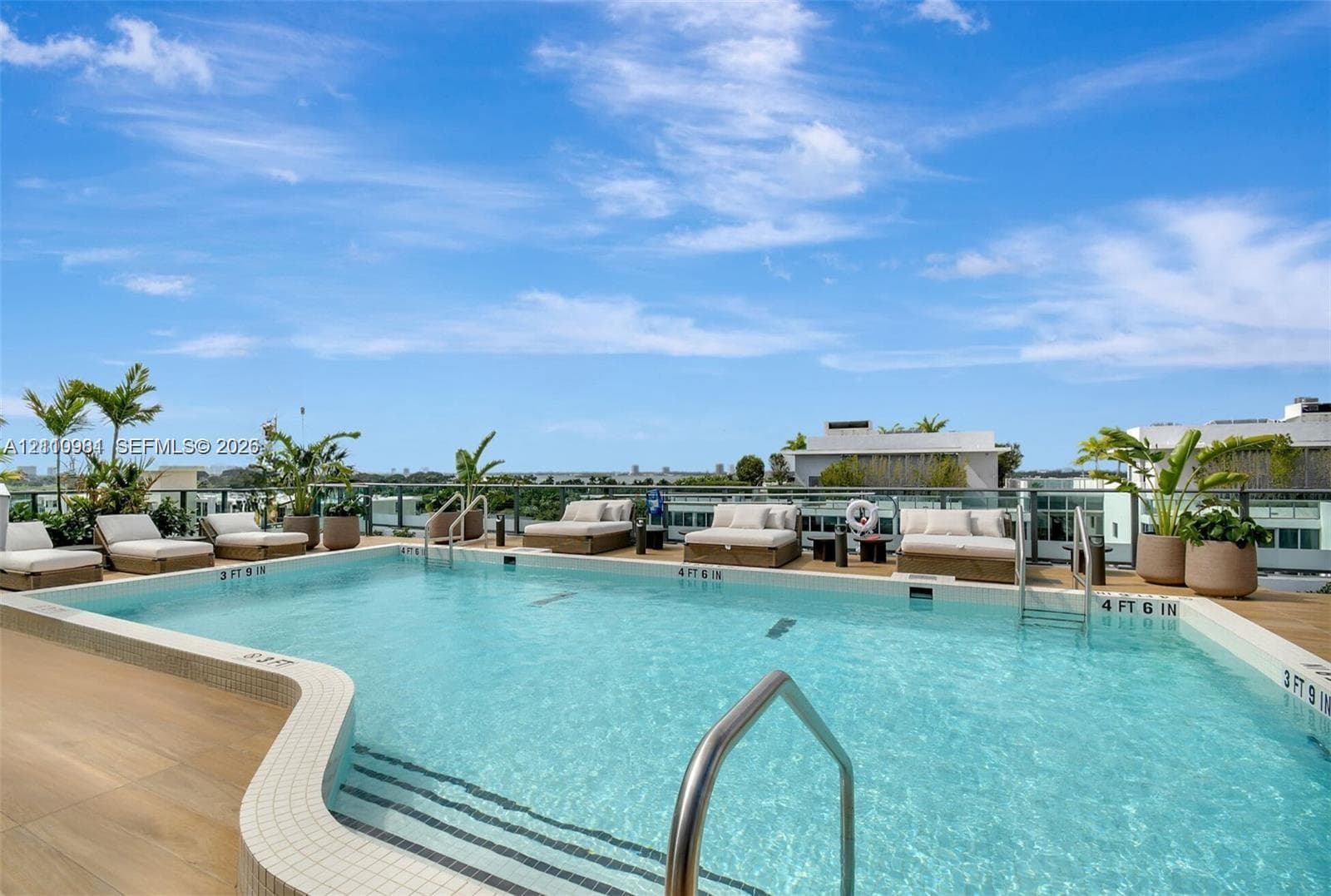 Rooftop swimming pool featuring wood-finish decking, tiled perimeter, metal handrails, and a glass paneled railing