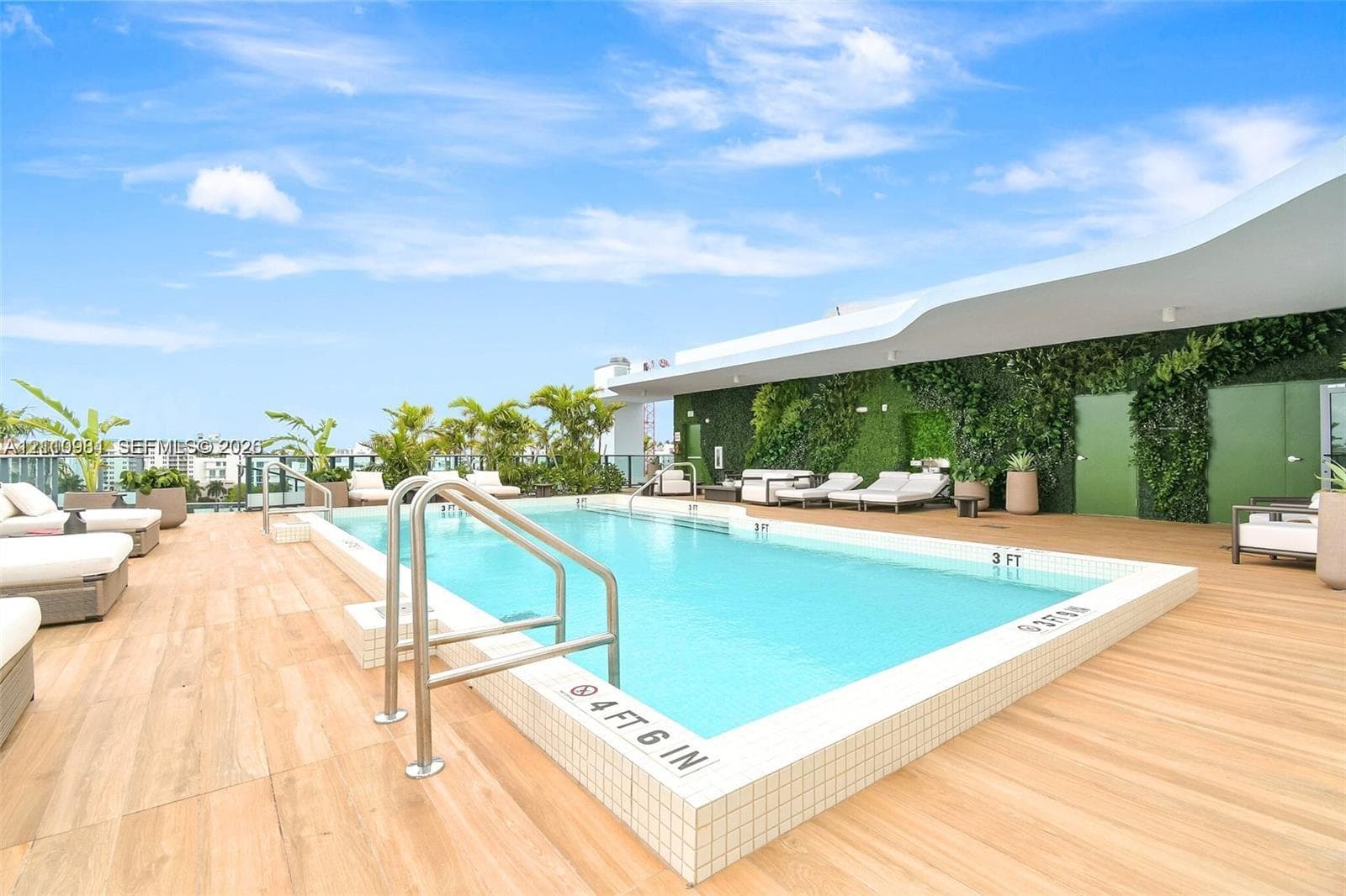 Rooftop swimming pool featuring wood-finish decking, vertical garden wall, and metal handrails