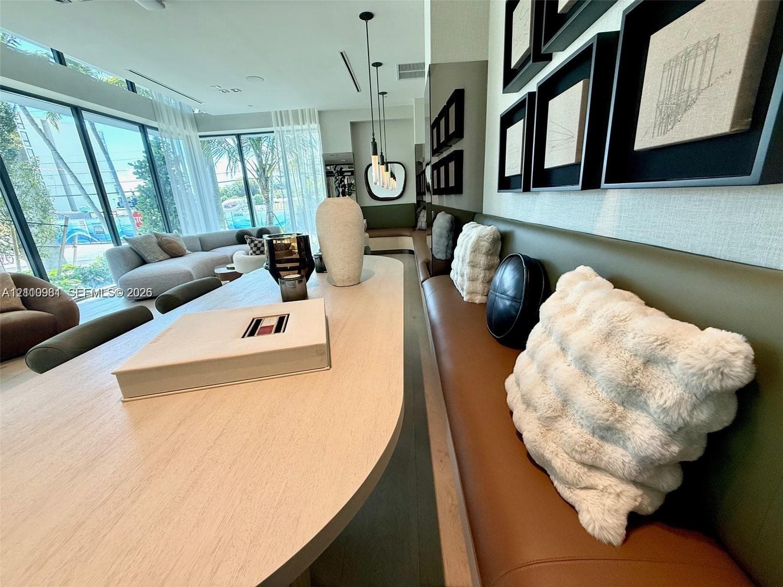 Floor-to-ceiling windows, built-in banquette seating with integrated upholstery, custom wood-finish table, and series of hanging pendant lights