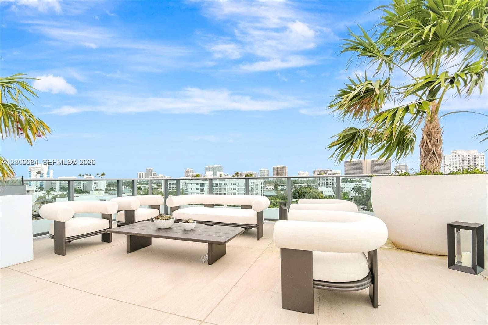 Expansive rooftop terrace featuring large-format stone tile flooring, a sleek glass railing system, and integrated palm tree planters