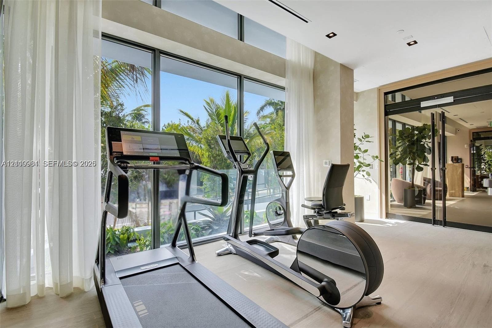 Floor-to-ceiling glass windows, recessed ceiling lighting, glass-paneled metal entry doors, and light-toned wood-finish flooring