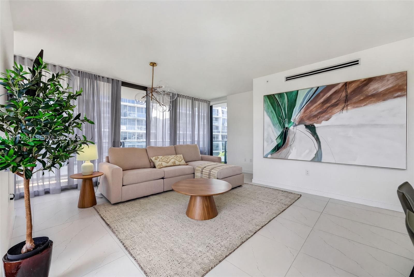 Living area featuring floor-to-ceiling glass paneling, large-format tile flooring, a multi-arm modern chandelier, and a recessed ceiling-mounted linear HVAC vent