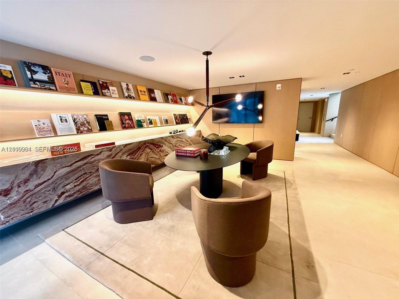 Custom built-in shelving with integrated lighting, stone-finish cabinetry, neutral large-format flooring, and modern multi-arm pendant lighting