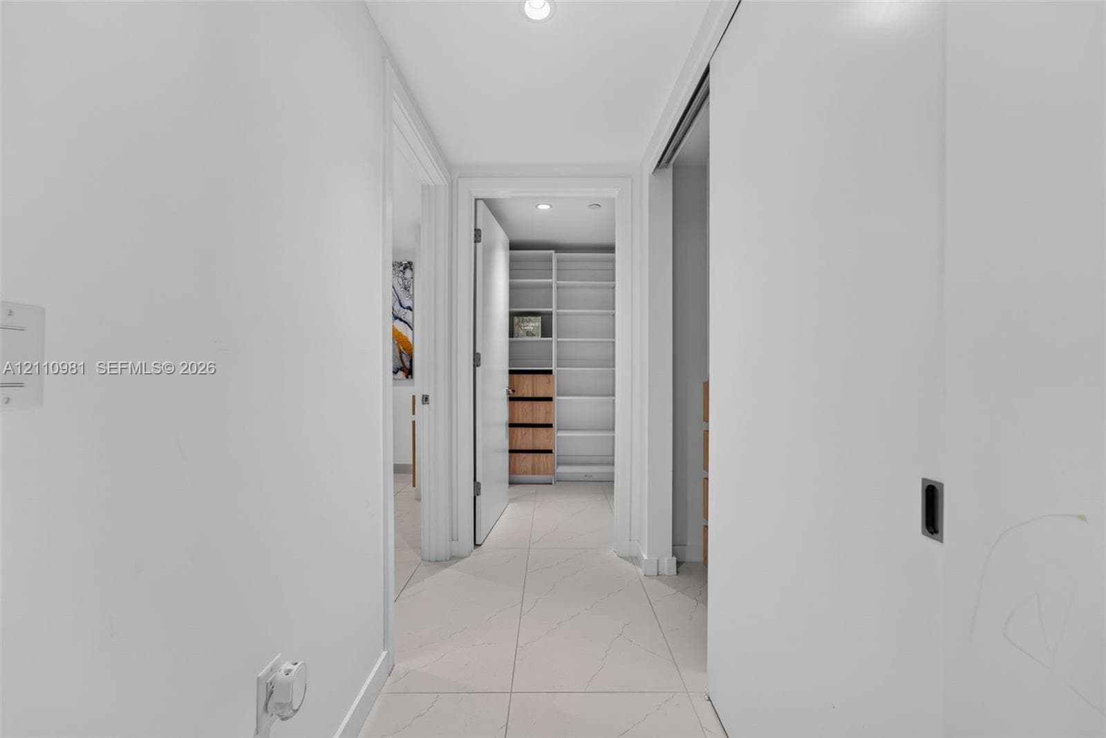 Hallway featuring large-format tile flooring, crisp white interior finishes, recessed lighting, and a custom built-in closet system with integrated shelving and drawer storage