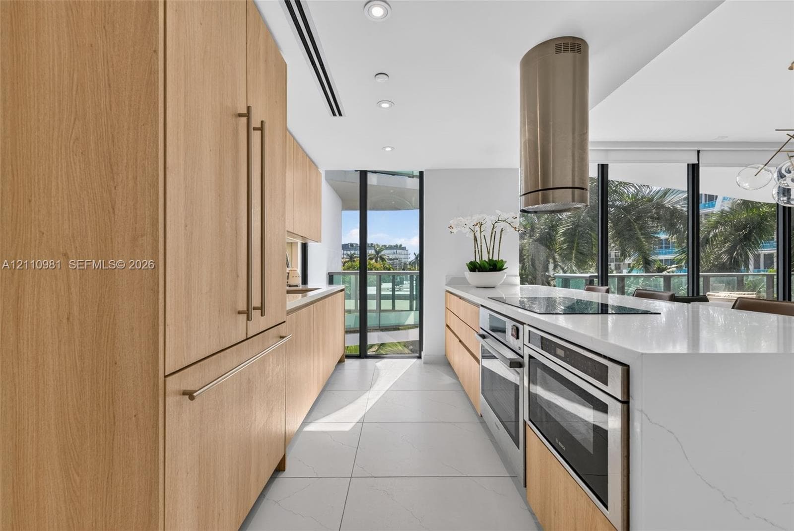 Kitchen featuring flat-panel wood-finish cabinetry, quartz countertops, an integrated cooktop with a cylindrical stainless steel range hood, dual built-in wall ovens, and porcelain tile flooring