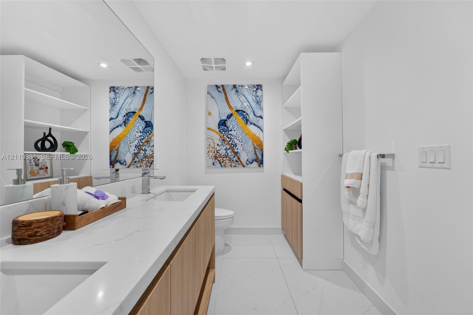 Double vanity with quartz countertop, light wood cabinetry, white tile flooring, and integrated wall shelving