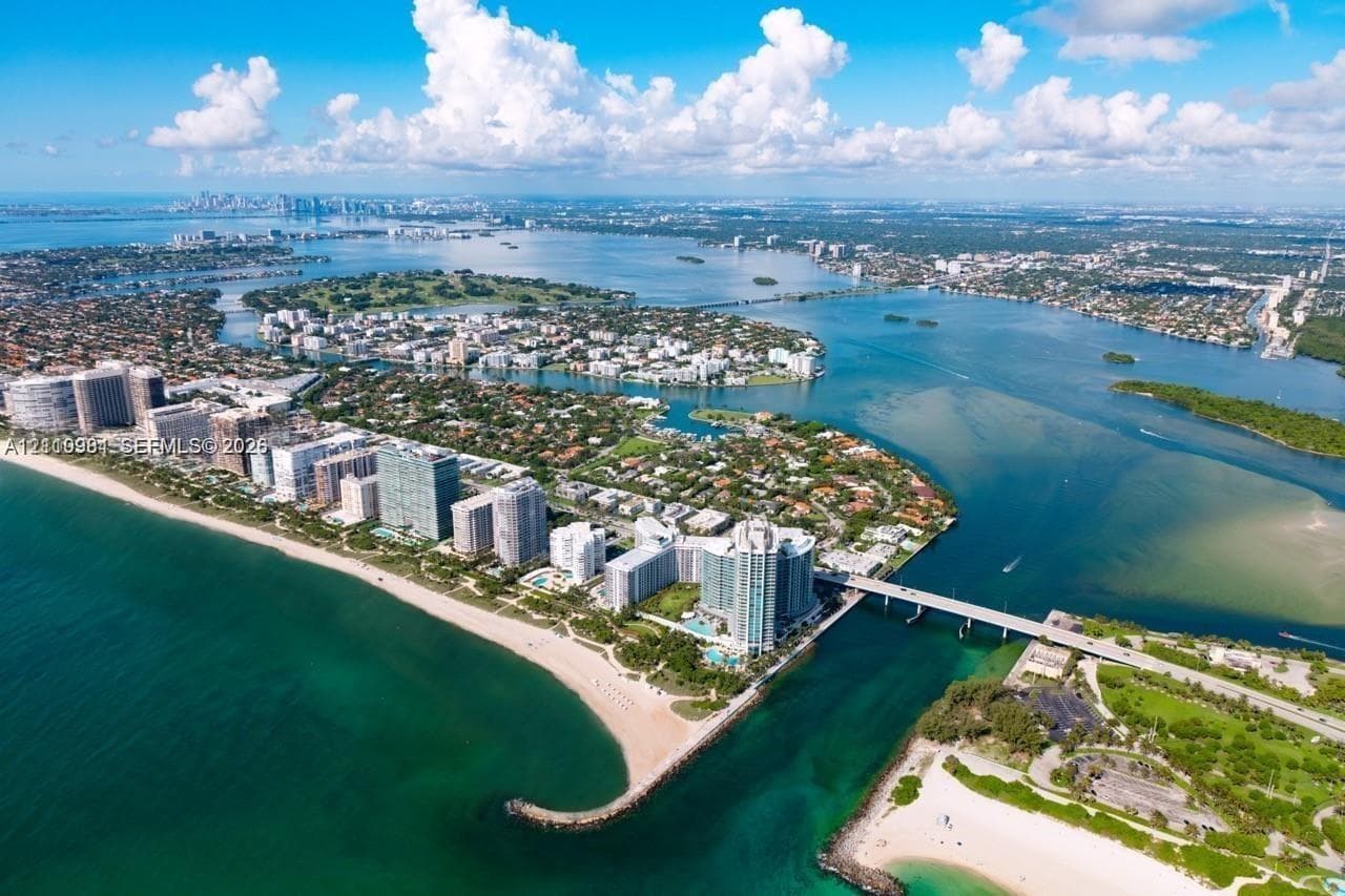 Aerial perspective featuring coastal waterfront positioning, expansive ocean and bay access, sandy shoreline, and multi-story high-rise structures