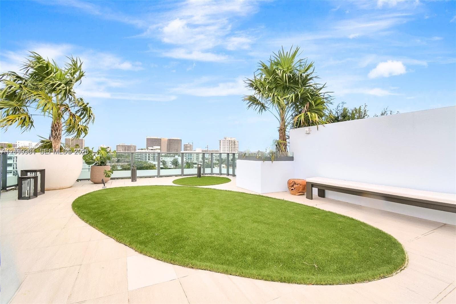 Rooftop terrace featuring large-format tile flooring, integrated artificial turf lawn, built-in bench seating, and glass panel perimeter railing