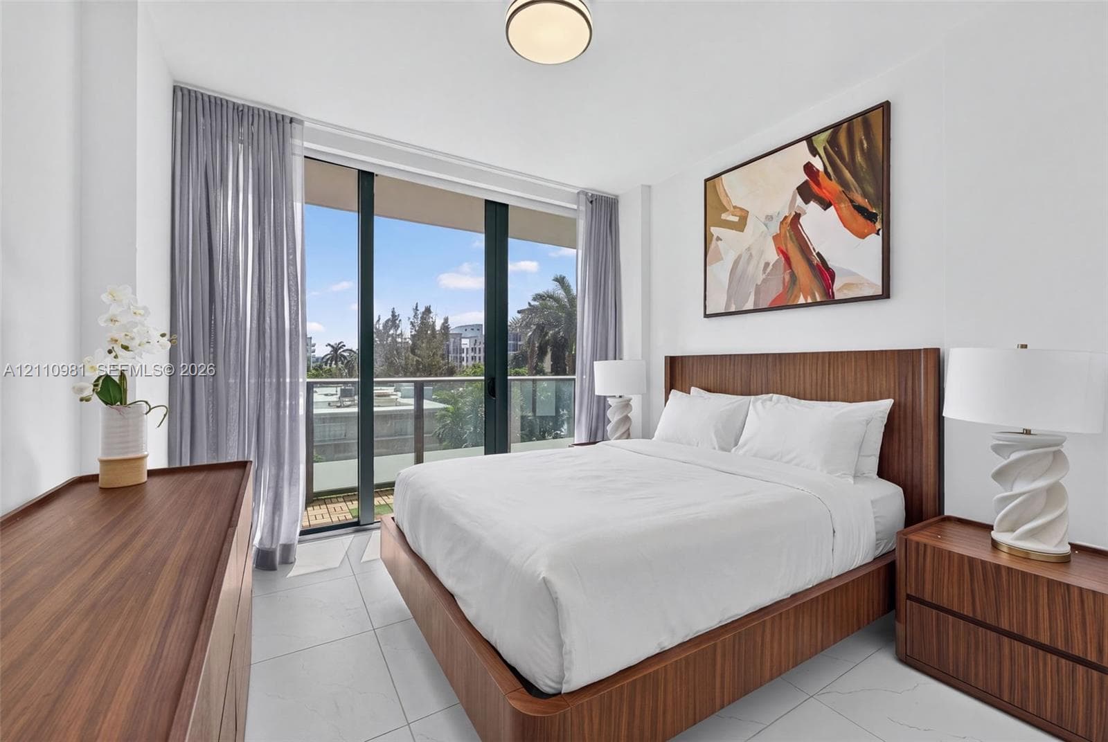 Floor-to-ceiling sliding glass doors, private balcony, neutral large-format tile flooring, and flush-mount lighting