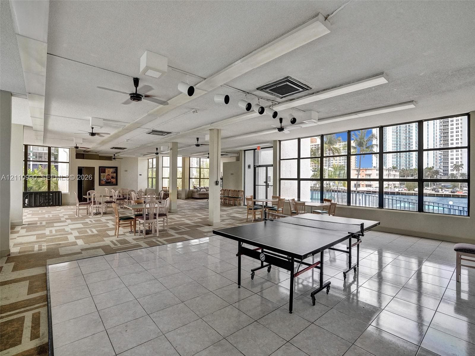 Open-concept interior featuring extensive floor-to-ceiling windows, ceramic tile flooring, patterned carpet, industrial-style track lighting, and ceiling fans