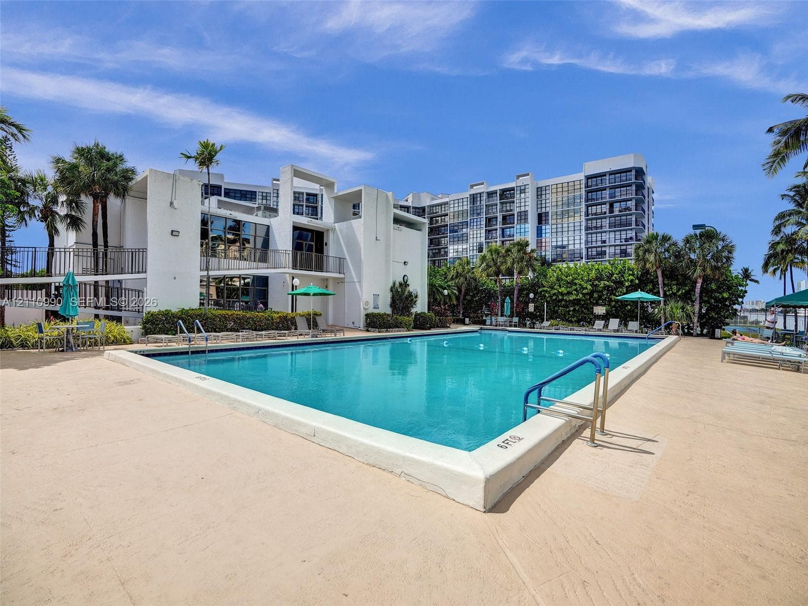 Outdoor swimming pool featuring a concrete deck, built-in metal handrails, and tropical landscaping