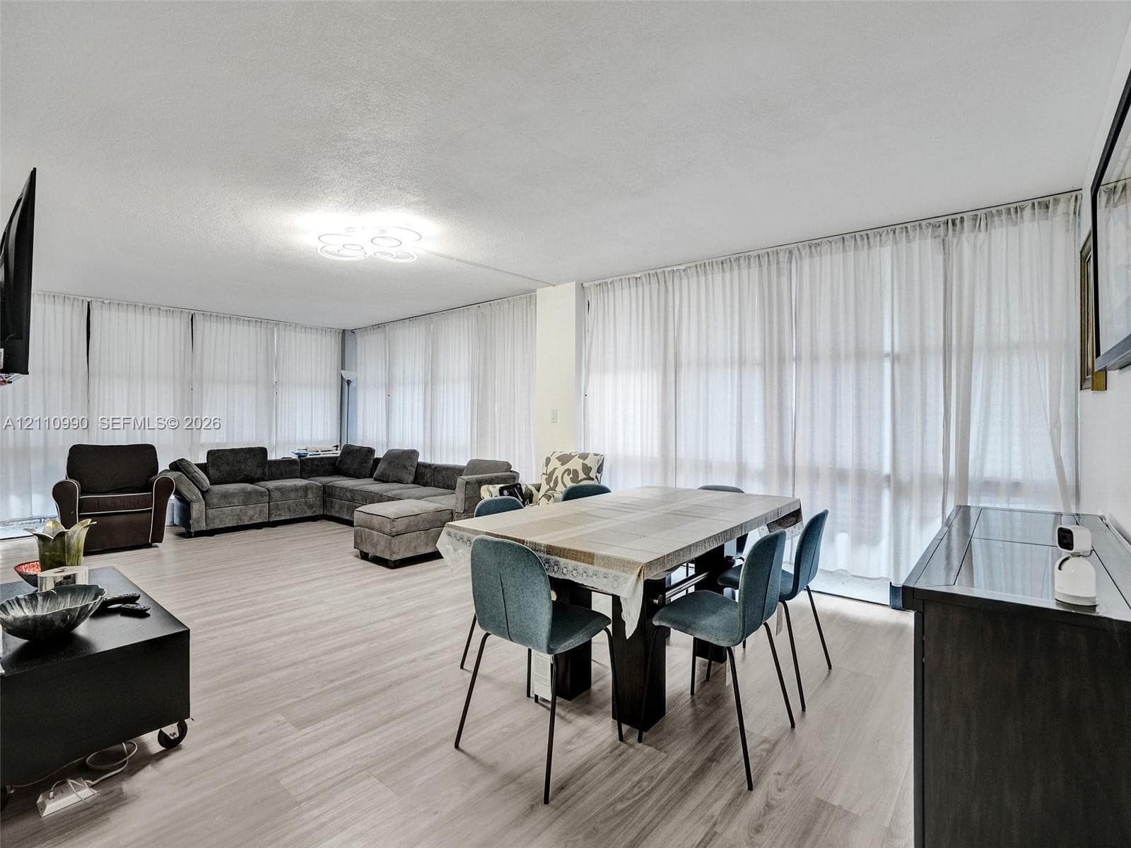 Open-concept living space featuring wood-finish flooring, floor-to-ceiling windows with window treatments, and an attached decorative ceiling light fixture