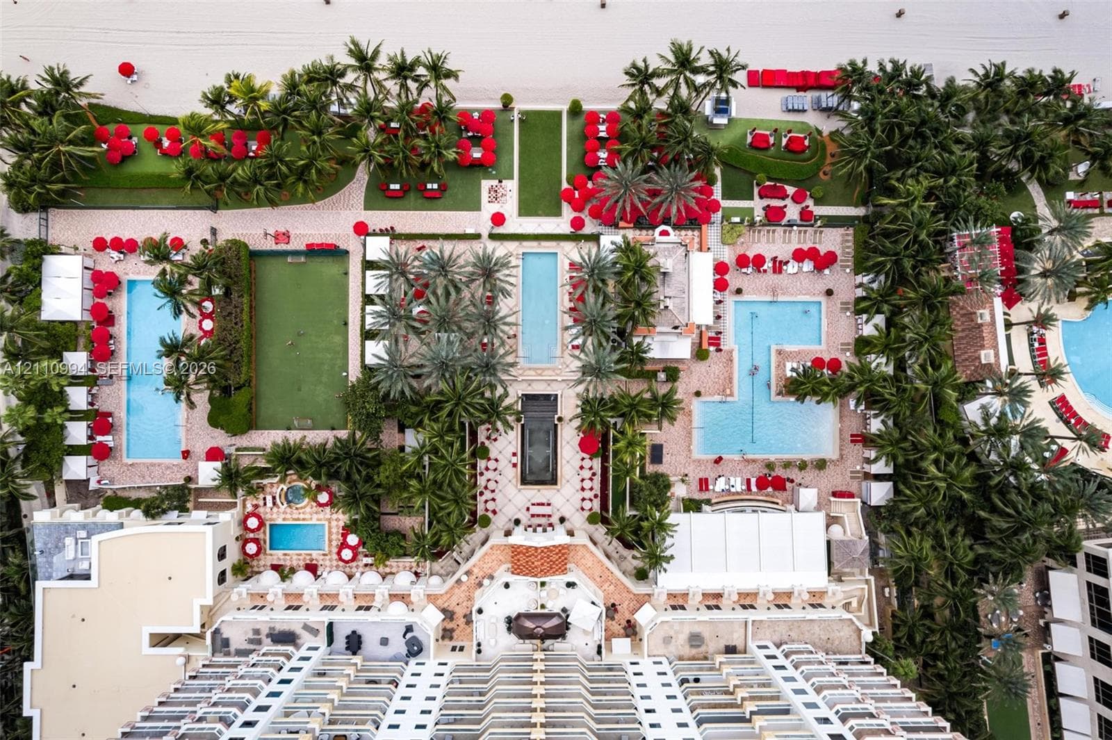 Aerial perspective featuring multi-level swimming pools, manicured palm landscaping, private putting green, and stone-paved courtyards with direct beach access