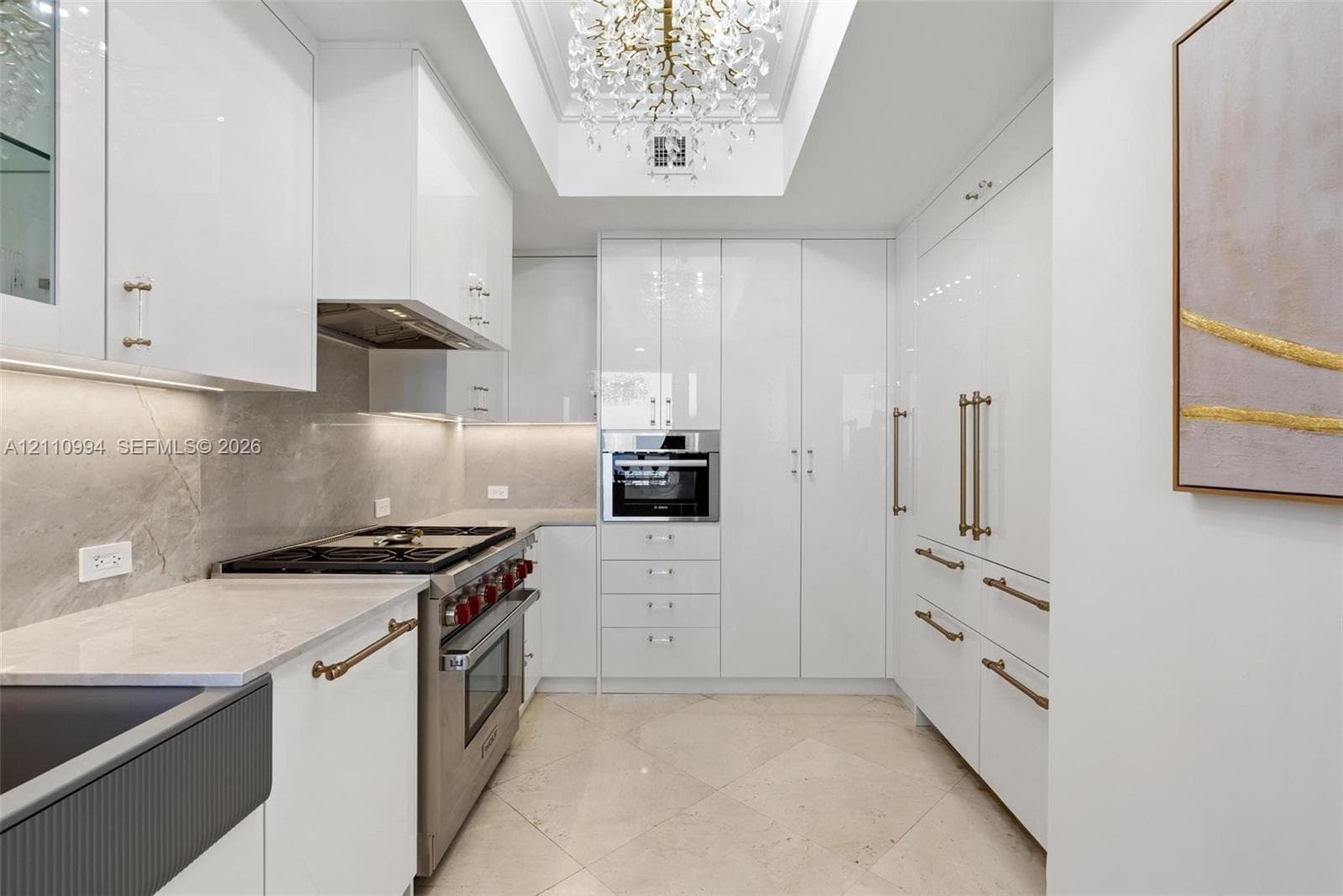 Gourmet kitchen featuring high-gloss cabinetry, stone-finish countertops, tile flooring, stainless steel professional-grade range, and a coffered ceiling with crystal chandelier