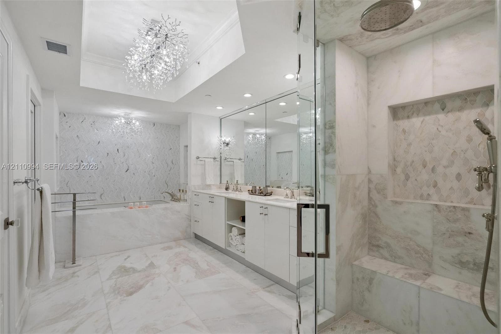 Bathroom featuring a white double-vanity, walk-in glass-enclosed shower with a built-in bench, soaking tub with decorative tile surround, and crystal chandelier lighting