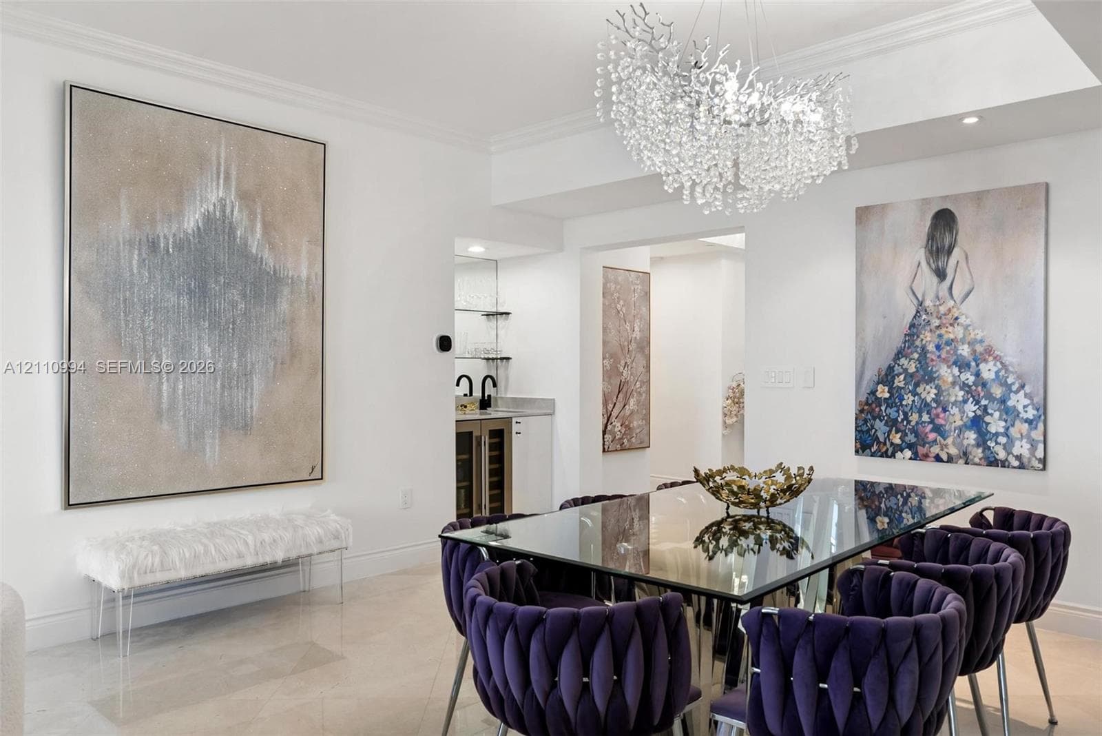 Statement chandelier with crystal accents, polished stone flooring, and a built-in wet bar featuring cabinetry, glass shelving, and a beverage refrigerator