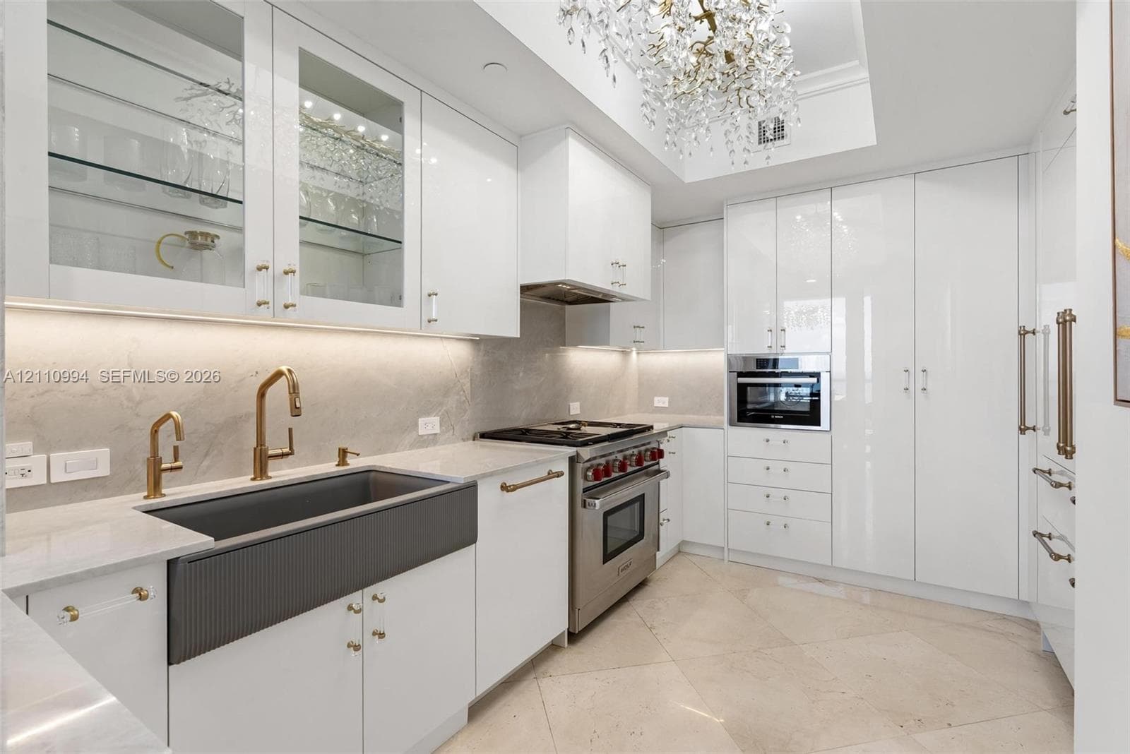 Kitchen featuring high-gloss cabinetry, stone-finish countertops, a dark-toned apron-front sink with gold-tone fixtures, stainless steel professional-grade range, and integrated appliances