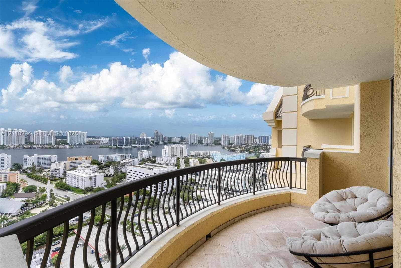 Covered balcony featuring tile flooring and a decorative metal railing overlooking the surrounding urban and waterfront landscape