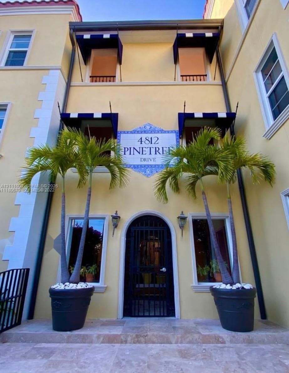 Stucco exterior featuring arched iron entry, decorative tile signage, blue-and-white fabric awnings, and stone-tiled steps