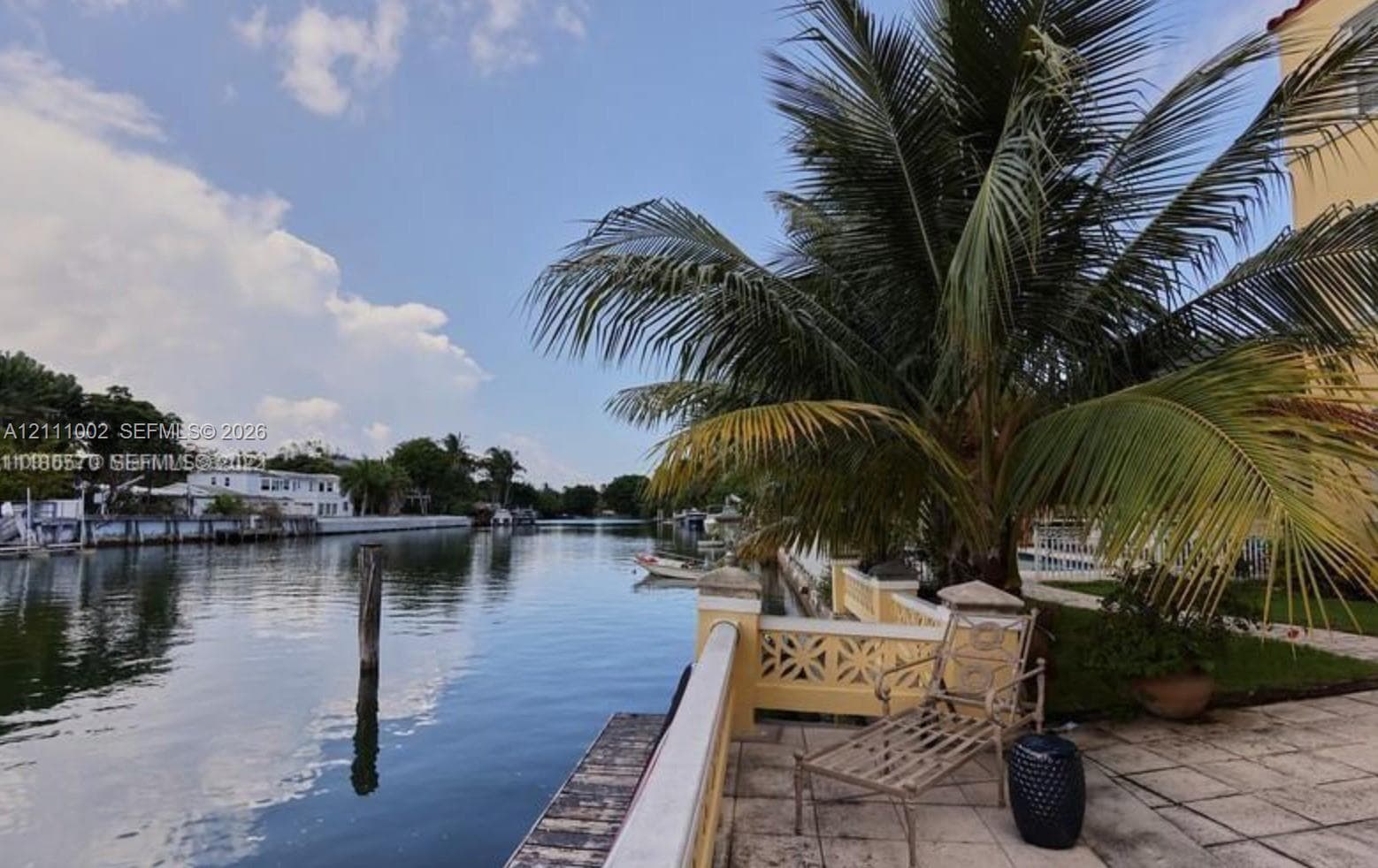 Waterfront terrace featuring stone paving, decorative masonry railing, and mature palm landscaping