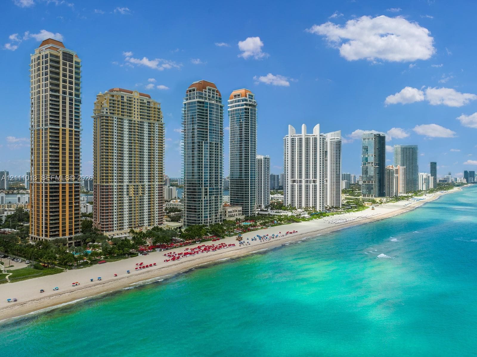 High-rise residential towers positioned along a sandy coastline featuring direct ocean access and expansive waterfront frontage