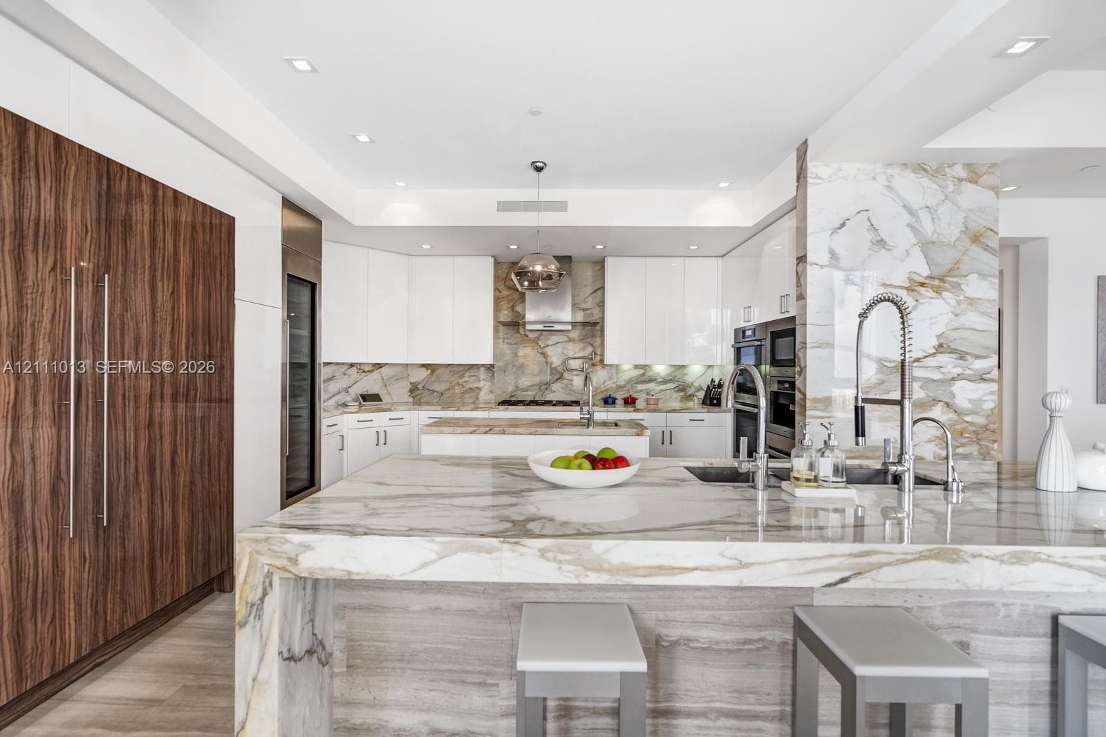 Kitchen featuring stone countertops and backsplash with waterfall edge island, high-gloss white cabinetry, integrated wood-finish paneled appliances, and stainless steel fixtures