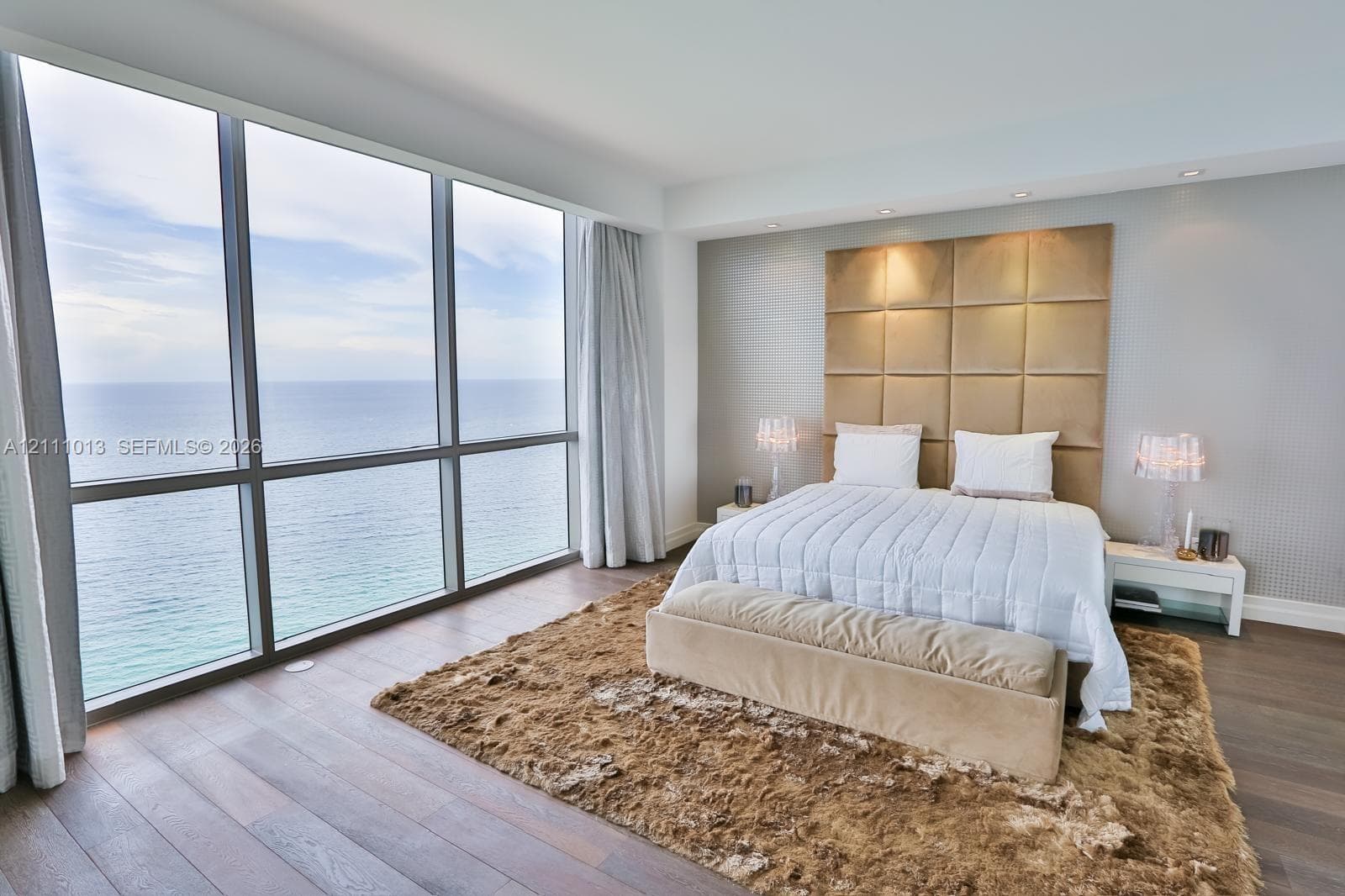 Floor-to-ceiling windows featuring ocean scenery, wood-finish flooring, and a floor-to-ceiling upholstered grid headboard