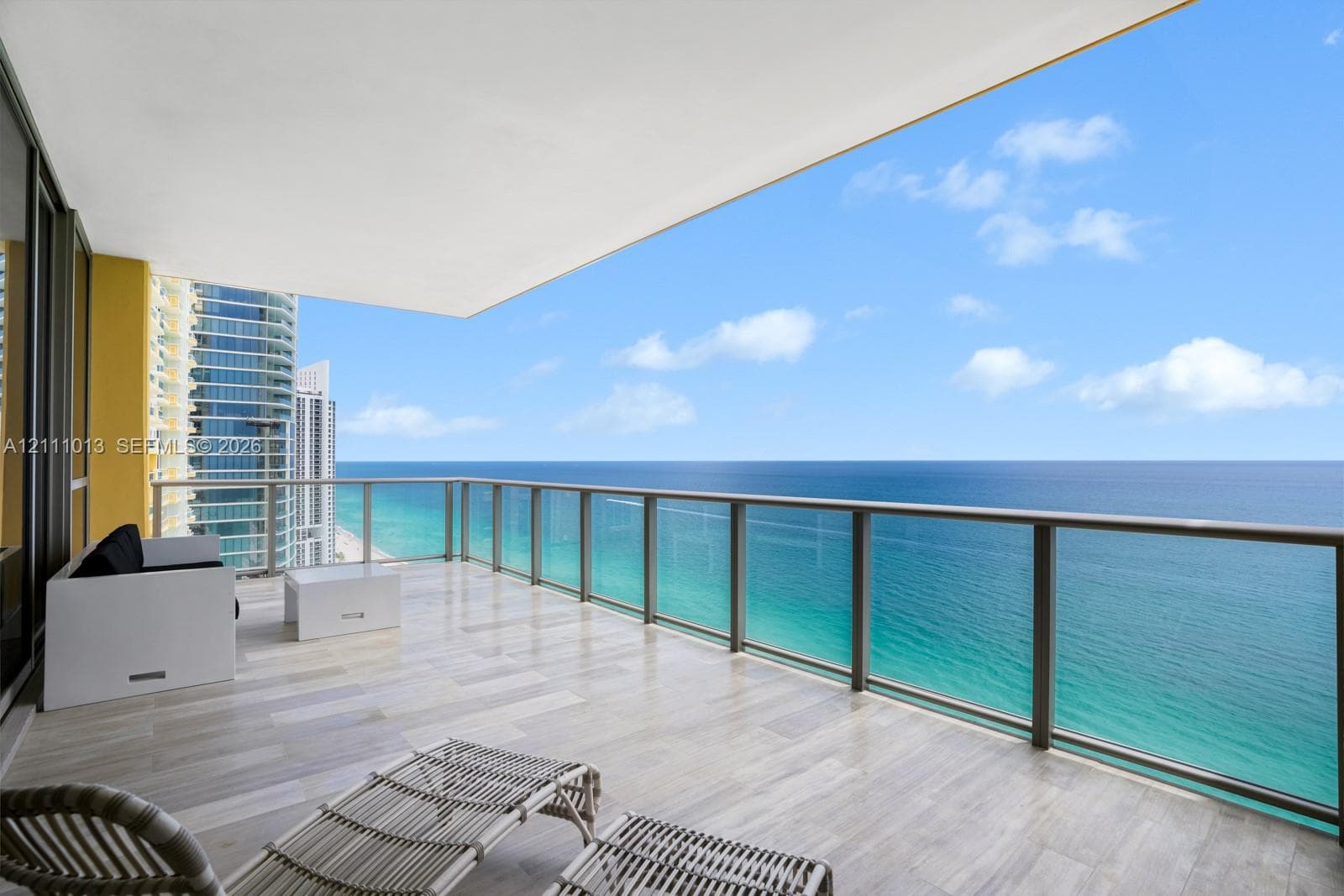 Covered balcony featuring tile flooring and a glass-paneled railing overlooking the ocean