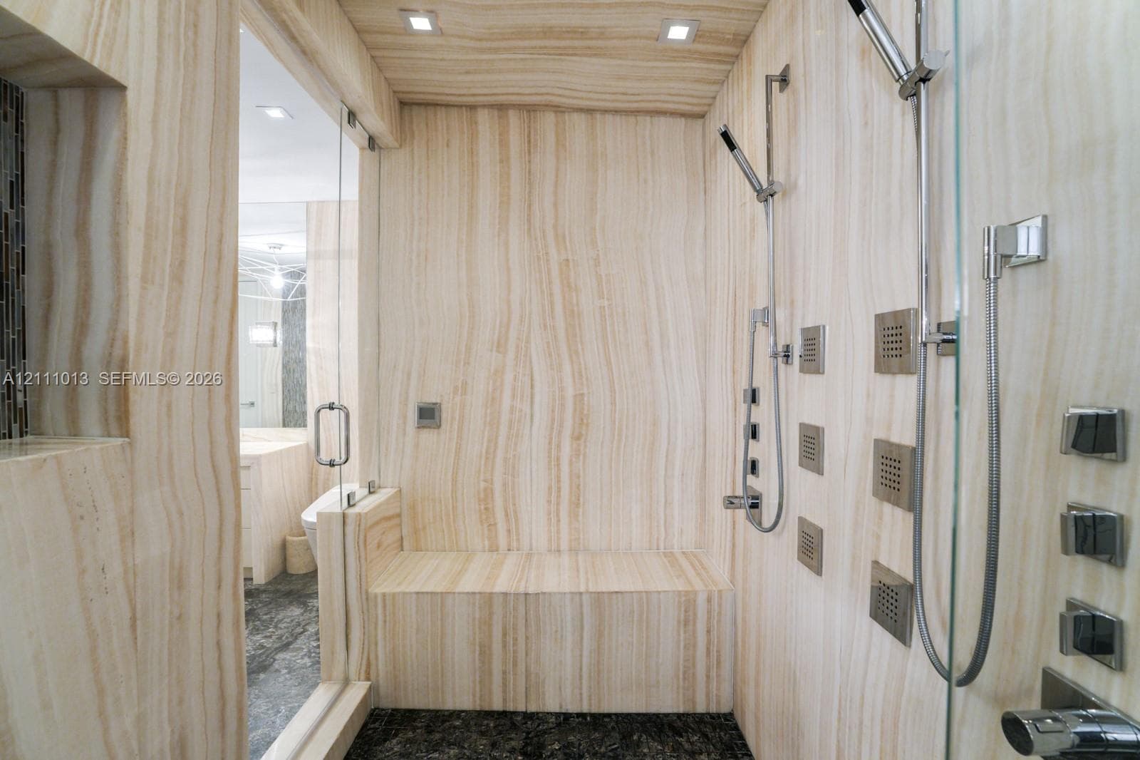 Walk-in shower featuring floor-to-ceiling stone wall cladding, built-in stone bench, multi-head chrome shower system, and frameless glass enclosure