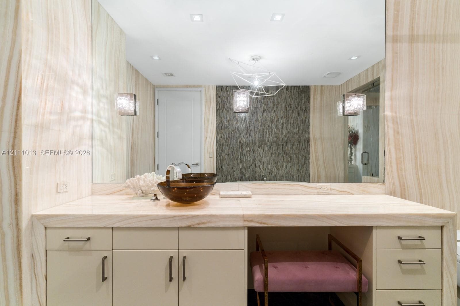 Custom vanity featuring a slab stone countertop, vessel sink, floor-to-ceiling stone wall cladding, geometric chandelier, and recessed lighting