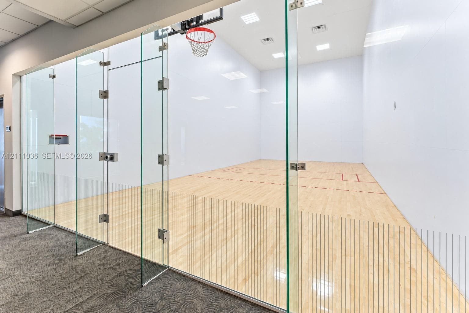 Recreational court featuring frameless glass wall enclosures, high-contrast wood-finish flooring, recessed ceiling lighting, and a built-in basketball hoop