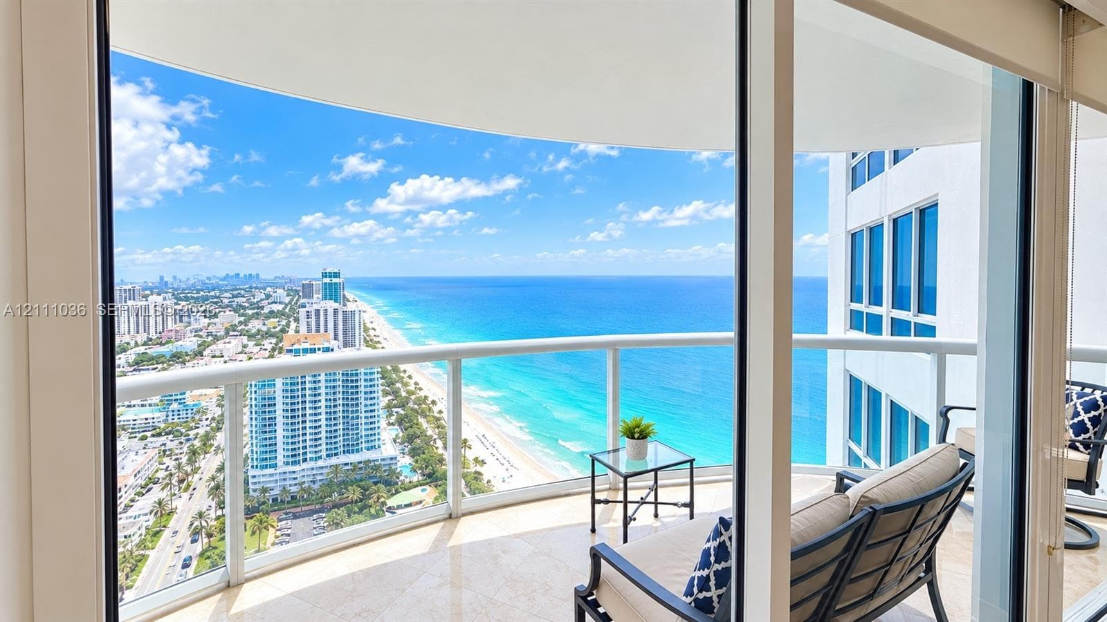 Covered wrap-around balcony featuring glass panel railings, stone flooring, and expansive coastal and urban scenery