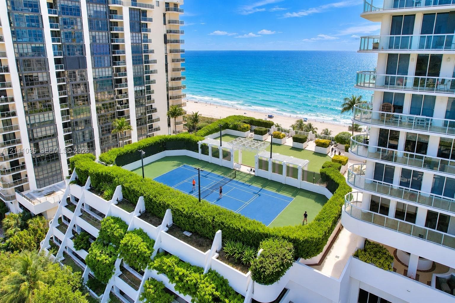 Rooftop recreational level featuring a tennis court, synthetic grass lawn area, perimeter hedge landscaping, and white pergola structures