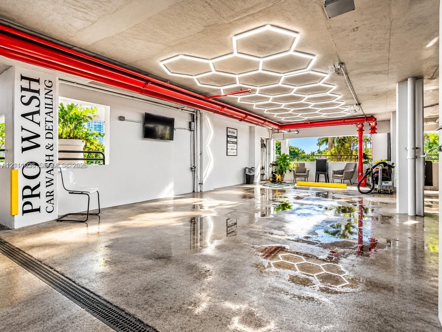 Car wash and detailing station featuring custom hexagonal overhead lighting, industrial concrete flooring, and an integrated drainage system