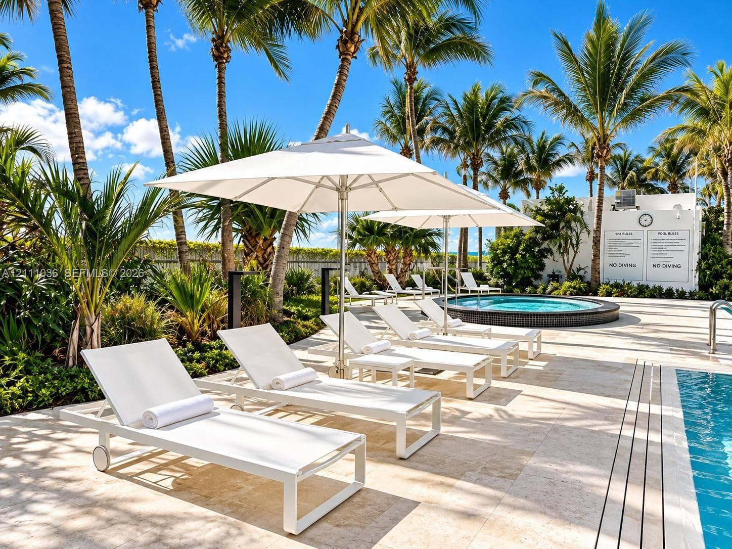 Outdoor pool area featuring natural stone decking, a circular jetted spa, and mature palm landscaping