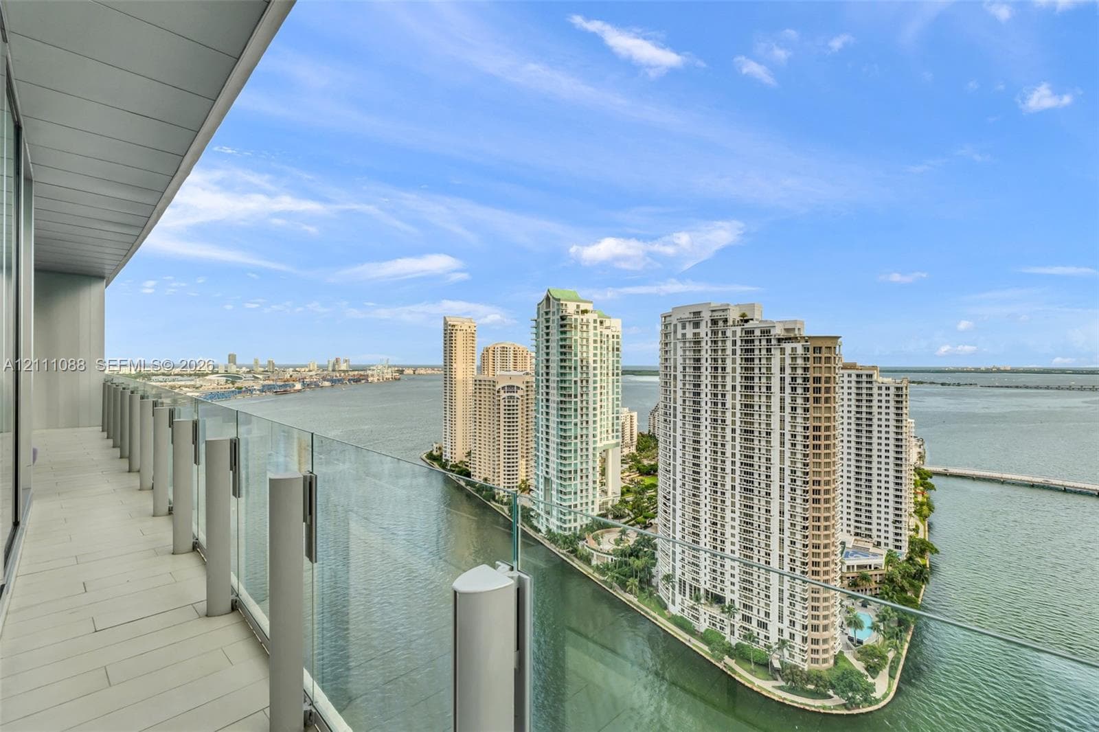 Covered balcony with light-toned flooring, frameless glass balustrades, and expansive water and urban skyline scenery